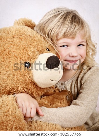 Little girl cuddling with her big plush teddy bear
