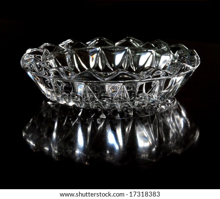 The engraved glass ashtray looks like a crystal king crown with reflection on the lacquered table.