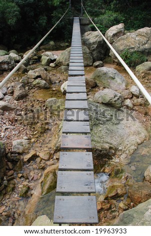 The pendant wood plank bridge with suspension cables over a mountain creek.