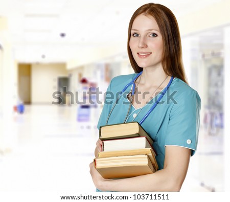 Smiling female doctor with books in a hall of a hospital