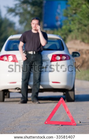 Young man calls to a service standing by a white car. Focus is on the red triangle sign