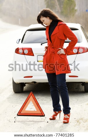 Young woman standing by the red triangle sign and her damaged car