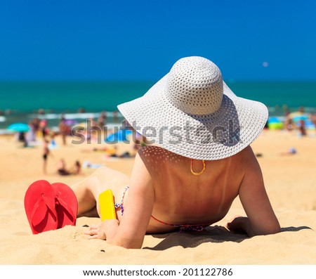 Woman sitting on a sandy beach, focus is on the flip-flops and bottle