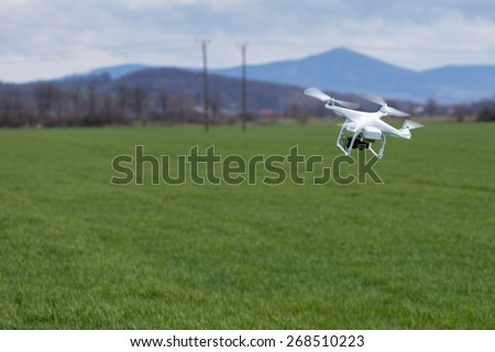 Small drone is flying high above the green field