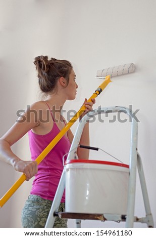 Young woman uses paint roller to apply paint on her new room. House decoration.