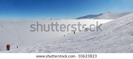 Skiers go down from mountain Stig in valley Dragobrat filled by a fog. On right in the distance mountain Bliznitsa, it is direct on background mountains Hoverla and Petros. Ukranian Carpathian region.