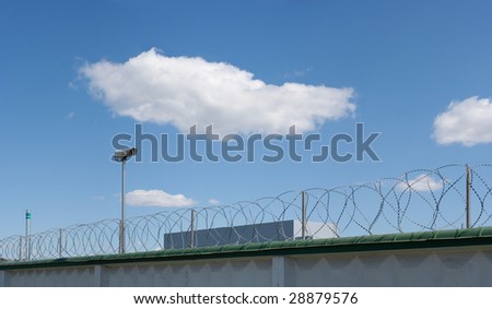 Surveillance camera on the wall with barbed wire of plant on blue sky background