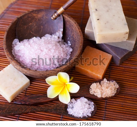 Spa set with handmade natural soap, sea salts in wooden bowl and frangipani flower.