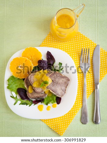 Boiled beef tongue with orange sauce and fresh salad on white plate and yellow fabric
