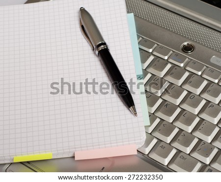 Photo of a white laptop, a notebook and a pen. Shallow depth of field, focus on the tip of the pen and the area nears it.