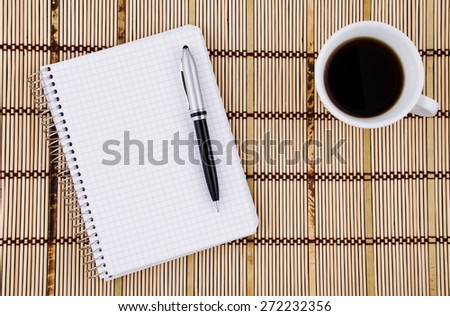 Blank page of notepad with pen and  coffee mug on bamboo mat background.