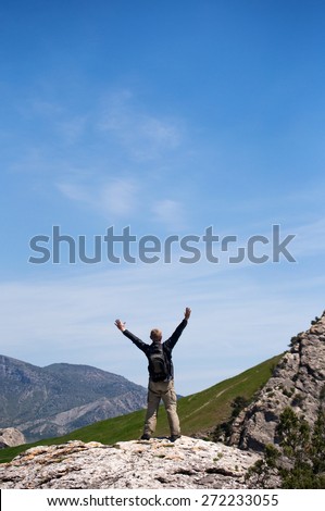 Happy man standing on the top of mount with his arms raised to the sky.