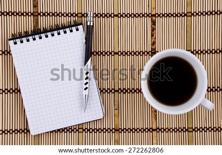 Blank page of notepad with pen and, coffee mug on bamboo mat background.