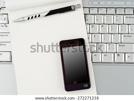 Photo of a silver laptop, a notepad, mobile phone and a pen.