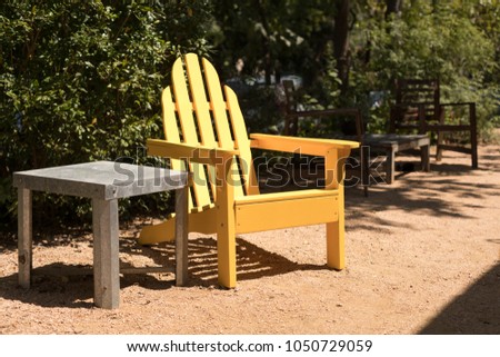 Side view on a yellow adirondack patio chair beside a metal table, in a bright outdoor patio and garden