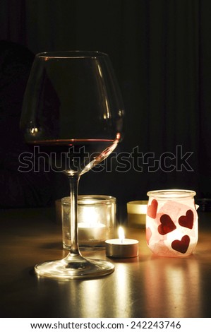 A glass of red wine, illuminated by a few candles, setting a romantic atmosphere