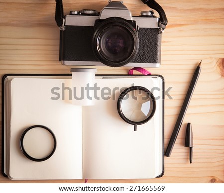 Retro vintage old photo camera with roll, lenses, notebook and pen on a wooden table