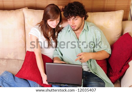 Young couple sitting on a couch looking at a laptop computer.