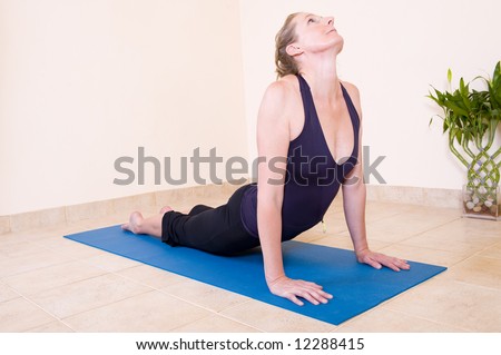 A beautiful mature lady in the \'Upward facing dog - Urdhva mukha\' yoga position, wearing a black outfit on a blue mat.