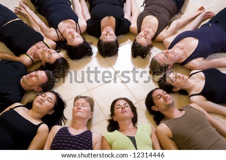 Yoga class relaxing in the \'Corpse pose - savasana\'. The group is lying in a circle with heads to the inside.