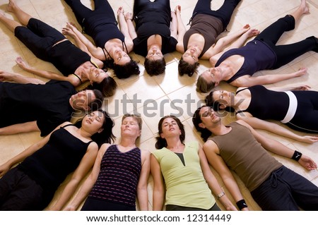 Yoga class relaxing in the \'Corpse pose - savasana\'. The group is lying in a circle with heads to the inside.