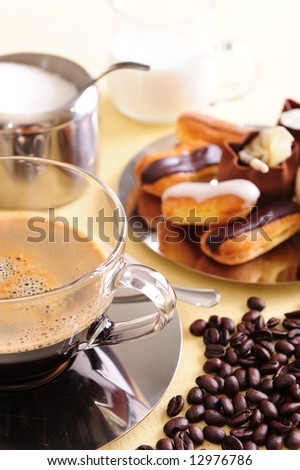 Freshly brewed coffee with a selection of pastries and cakes.  Coffee beans scattered next to the cup for extra effect.