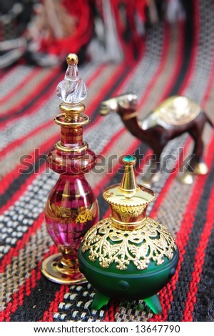 Egyptian perfume bottles arranged on a hand-woven Omani rug. A small copper replica of a camel is faded in the background.