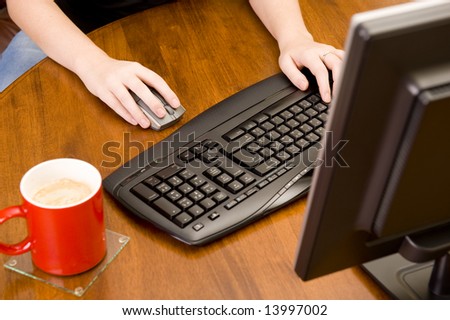 Female executive working on a PC keyboard and/or mouse on a wooden desk.