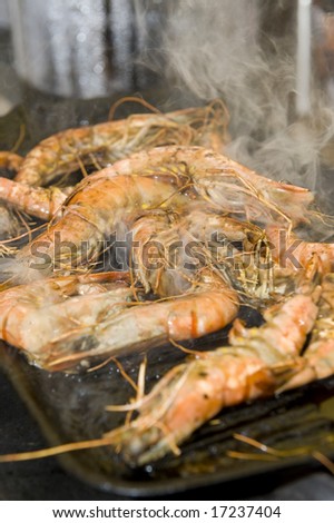 Smoking prawns cooking on an iron barbecue plate.