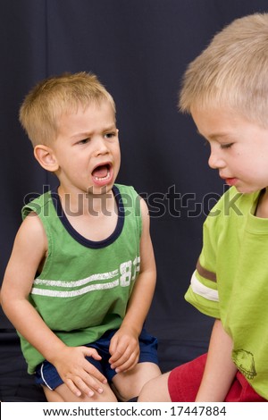 A cute little 3 year old boy shouting angrily at his 5 year old brother.