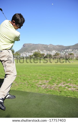 A golfer in action on a practice or driving range, hitting the ball with a club.