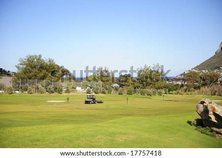 A beautifully maintained practice or driving range with distance markers for golfers to practice on. A motorized vehicle is in the process of picking up balls on the range.