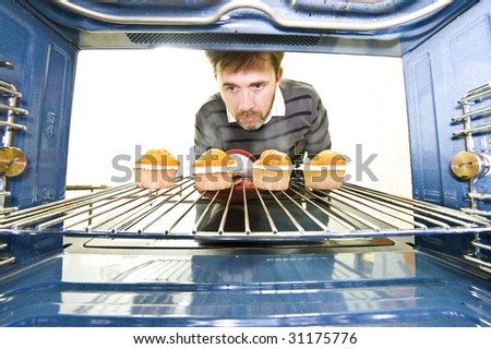 A unique viewpoint from inside an oven while a man removes some freshly baked cupcakes.
