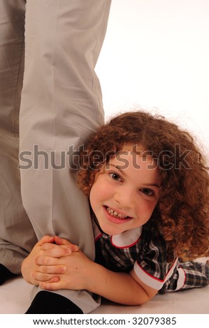 An adorable little girl with very curly hair holding on to her daddy's leg.
