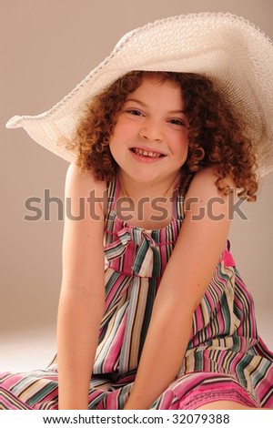 An adorable little girl with very curly hair, wearing a wide-brimmed sun hat.