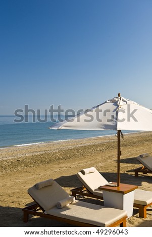 Deck chairs under an umbrella next to the beach on a sunny day.