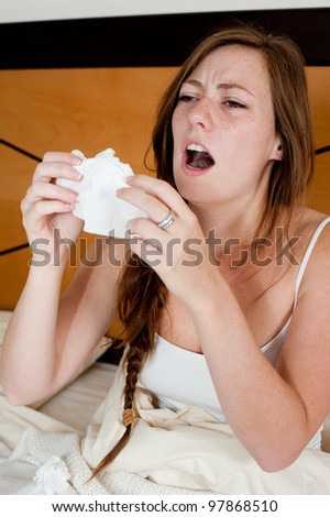 A sick young lady in bed, holding a tissue in front of her face to stop a sneeze.