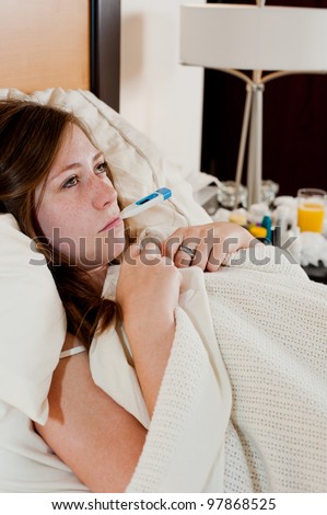 A sick young lady in bed, using a thermometer to check her temperature for fever.