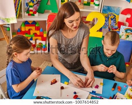 Plasticine modeling clay in children class. Teacher teaches kids together play dough and mold from plasticine in kindergarten or preschool. Educational childhood play room.