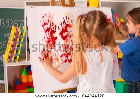 Children painting finger on easel. Group of kids girl and boy with teacher learn paint in class school. Child picture on background. Unusual ways of drawing.