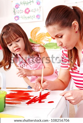 Child and teacher painting at easel in school.