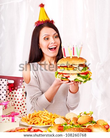 Woman wearing party hat eating hamburger at birthday.