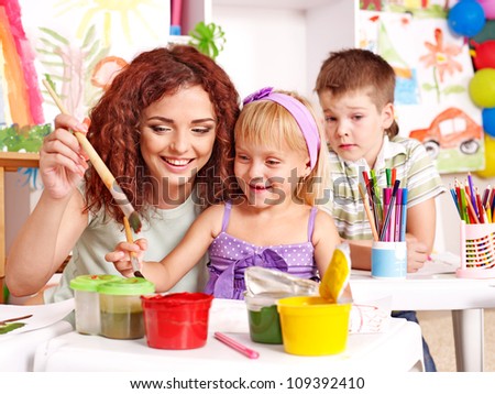 Children with teacher painting at easel in school.