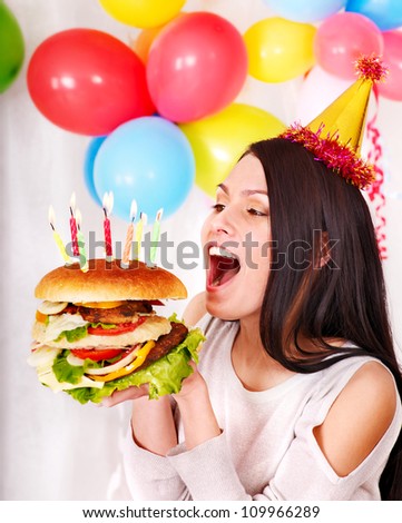 Woman wearing party hat eating hamburger at birthday.