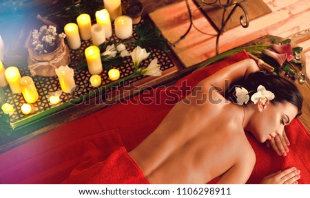 Massage of woman in spa salon. Girl on candles background in massage spa salon. Luxary interior in oriental therapy salon. Female have relax after sport. Top view and rays falling from above.