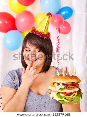 Overweight woman eating hamburger at birthday.
