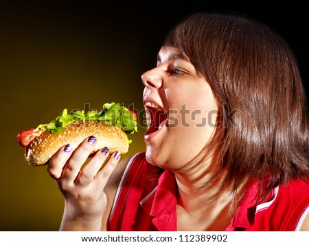 Overweight hungry woman eating hamburger.