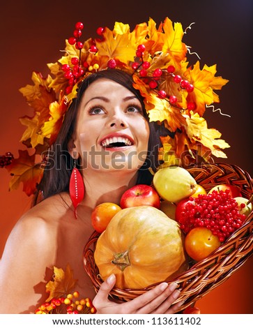Girl with wreath of autumn leaves holding basket with fruit.