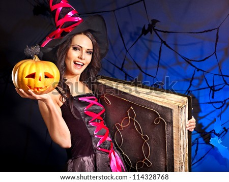 Happy witch woman holding old book and pumpkin.