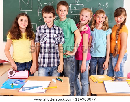 Group of school child sitting on desk in classroom.
